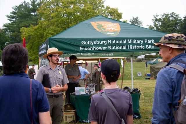 A park ranger meets a group of visitors to begin a walking tour. They stand in front of a tent that reads “Gettysburg national military park/Eisenhower National Historic Site Rangers provided guided walks throughout the weekend Keywords: Eisenhower; World War II; Living History. Walking tour companies: reading the replies before booking